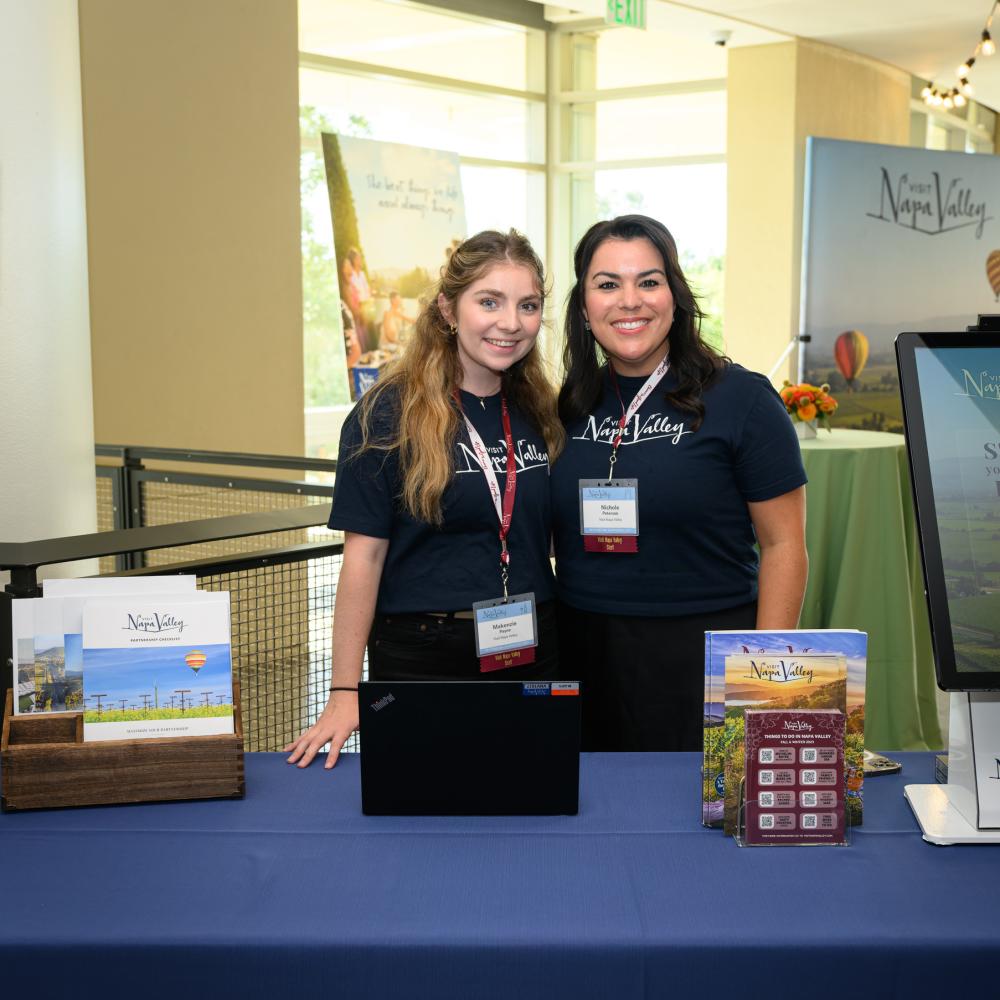 2 women behind a table at a conference with Partnership sign and collateral